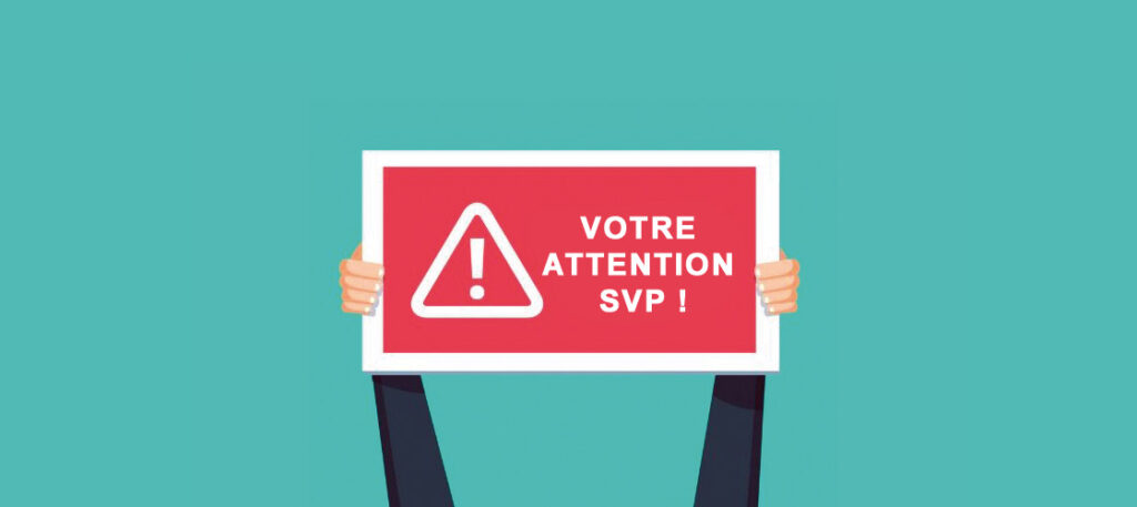 Votre attention s'il vous plaît, texte blanc sur pancarte rouge tenue par deux mains, le tout sur fond vert.
